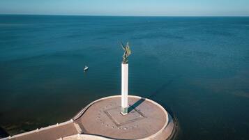 Vista aérea de un paseo marítimo con un monumento central, una plaza circular y un mar tranquilo.