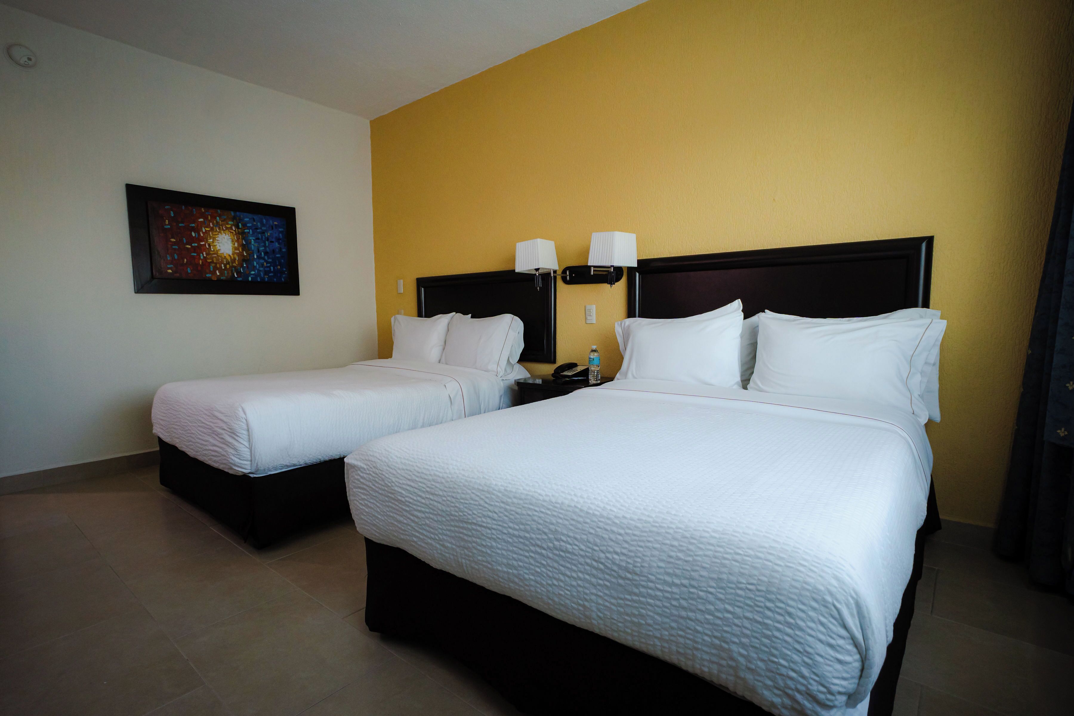 A hotel room with two beds, a nightstand, a lamp, and a wall-mounted painting.