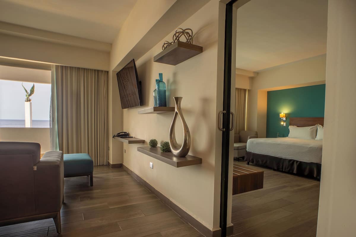 A hotel room with a bed, a sofa, a TV, a small table, and a window with curtains.