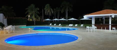 A swimming pool area with lounge chairs and umbrellas.