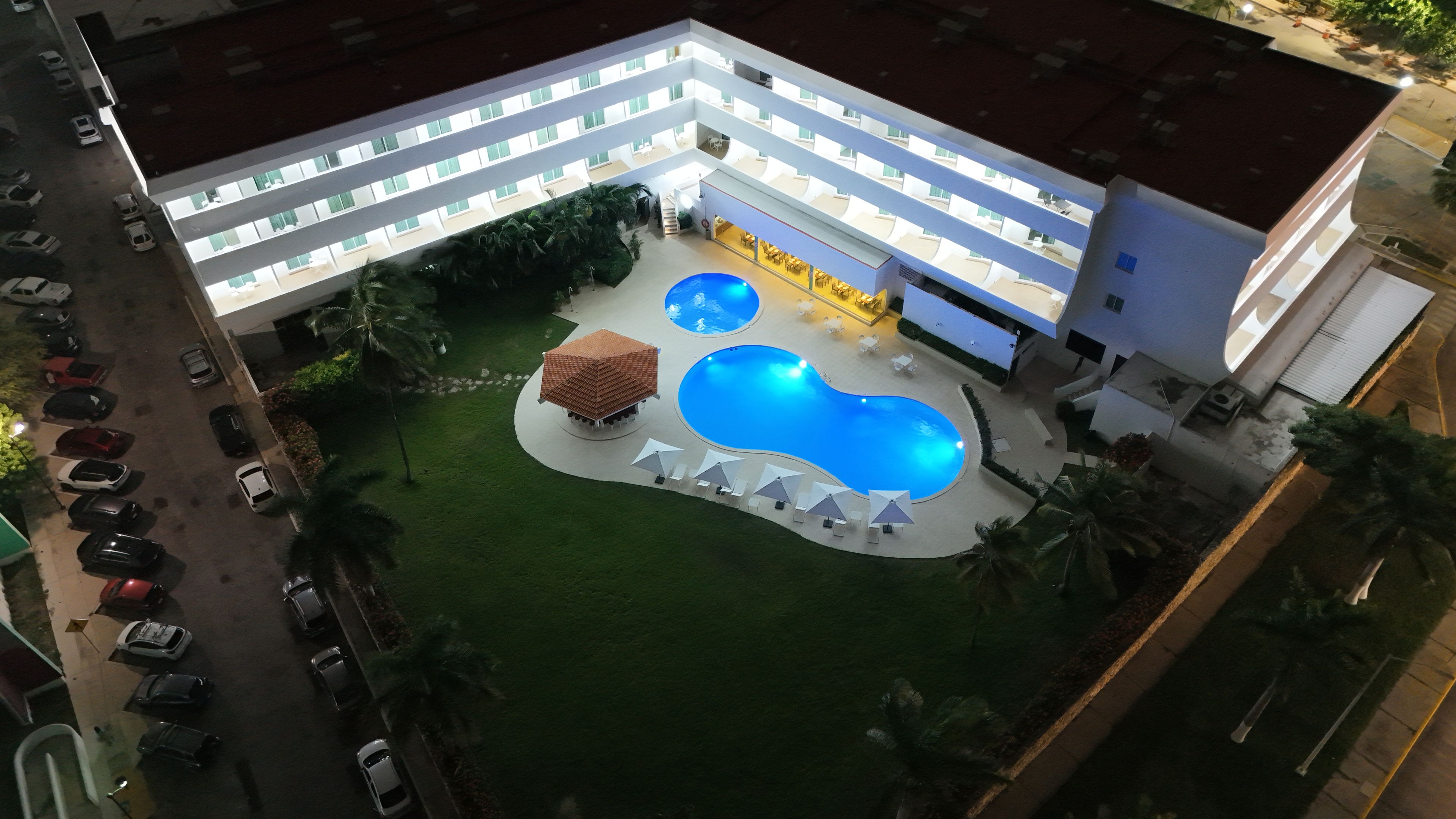 A hotel with a swimming pool, multiple floors, and a parking area.