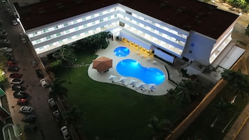 Un hotel con piscina, varias plantas y zona de estacionamiento.