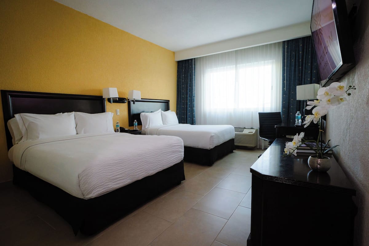 A hotel room with two beds, a desk with a TV, and a vase of flowers.