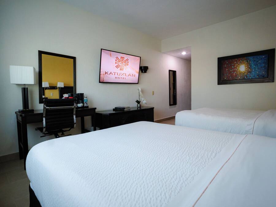 A hotel room with two beds, a desk with a chair, a desk lamp, a mirror, a framed sign, and a painting on the wall.