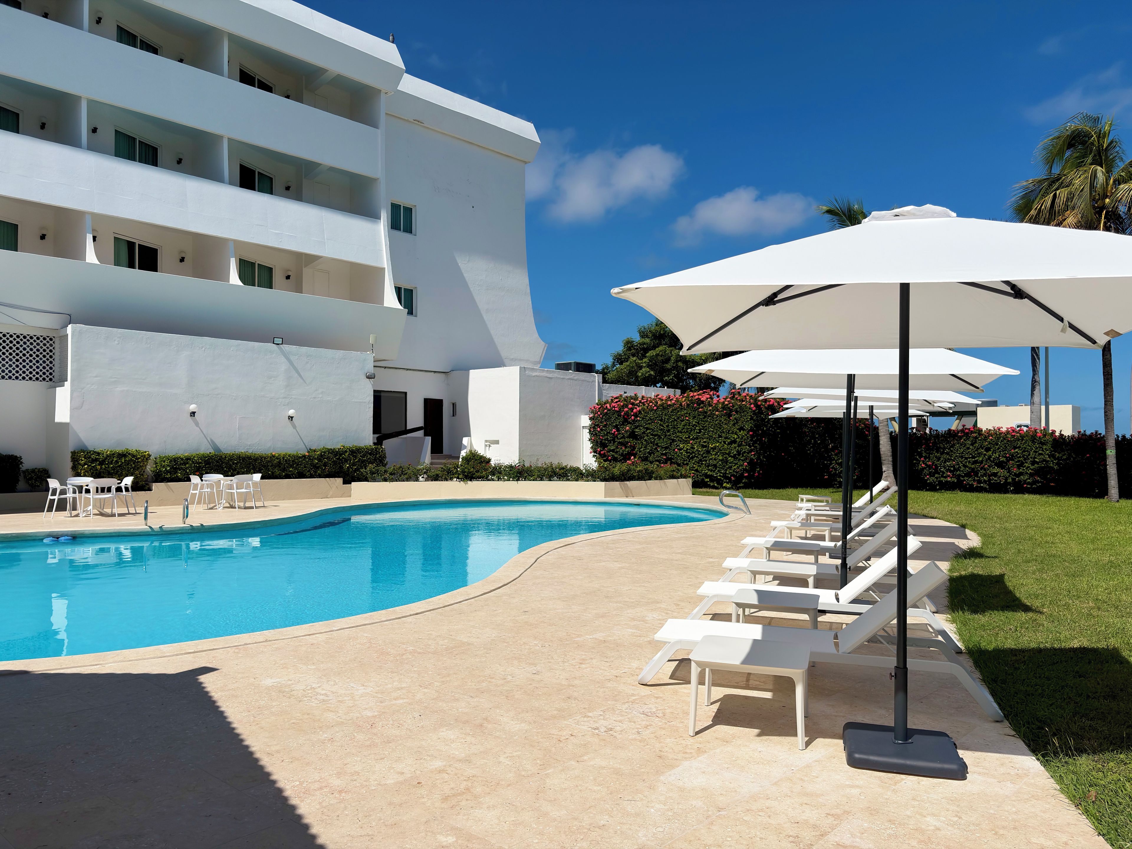 Ein Pool mit Liegestühlen und Sonnenschirmen, umgeben von einem modernen Gebäude mit Balkonen.