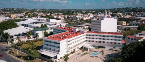 An aerial view of a cityscape with a prominent white building with a red roof, surrounded by smaller structures and greenery.