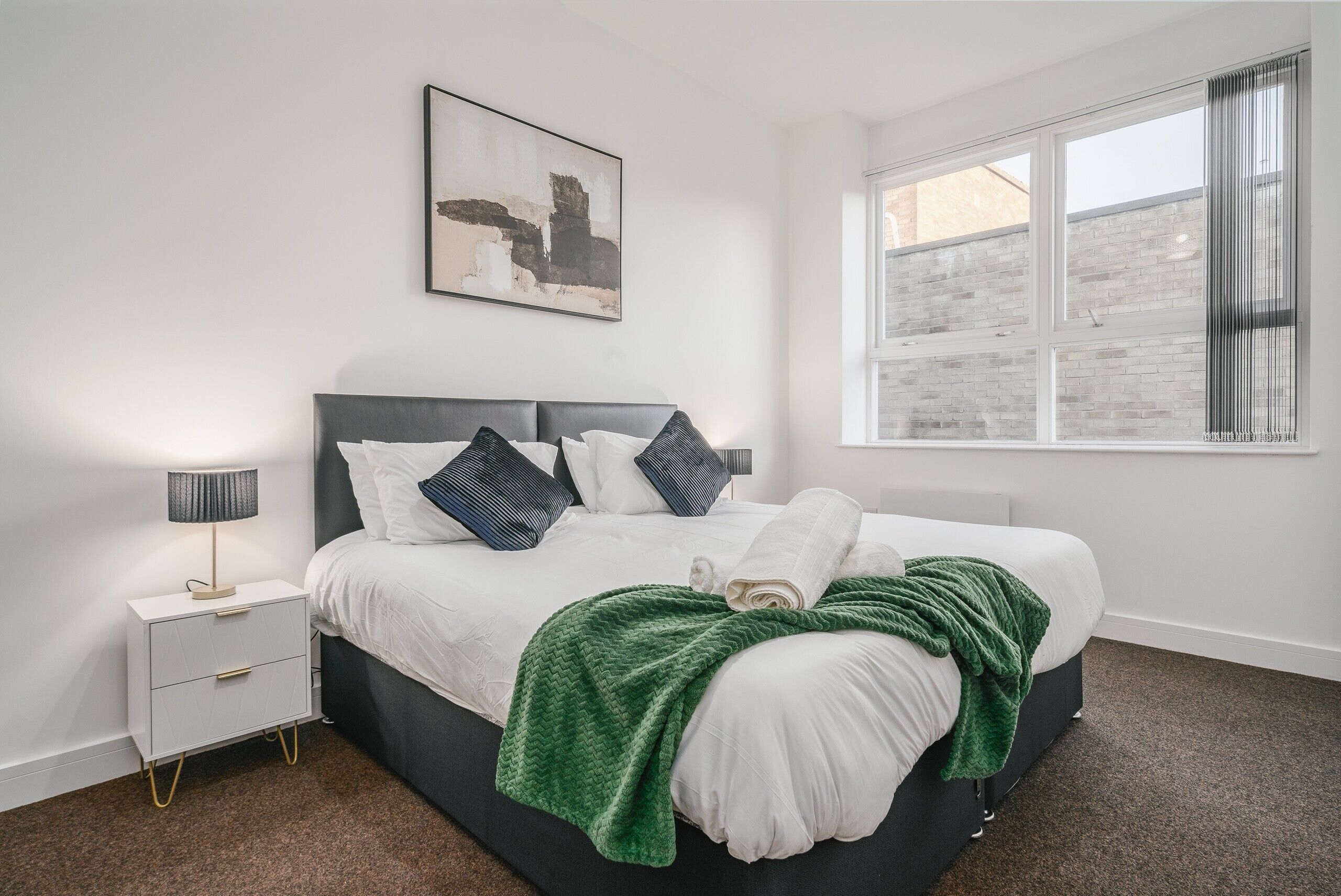 A bedroom with a bed, a nightstand, a window, and a wall-mounted artwork.