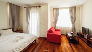 A hotel room with a bed, a red sofa, a TV, and a wooden floor. - Cozy 1BR condo with hardwood floors and rooftop sunset garden in Phnom Penh (Phnom Penh)