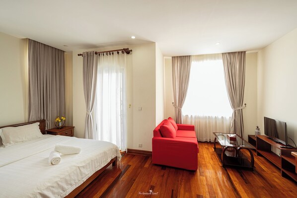 Une chambre d’hôtel avec un lit, un canapé rouge, une télévision et un plancher en bois.