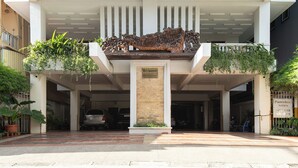 A hotel entrance with a decorative metal sculpture, a sign indicating available rooms, and a gated parking area. - Cozy 1BR condo with hardwood floors and rooftop sunset garden in Phnom Penh (Phnom Penh)
