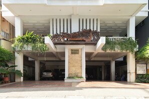 A hotel entrance with a decorative metal sculpture, a sign indicating available rooms, and a gated parking area. - Cozy 1BR condo with hardwood floors and rooftop sunset garden in Phnom Penh (Phnom Penh)