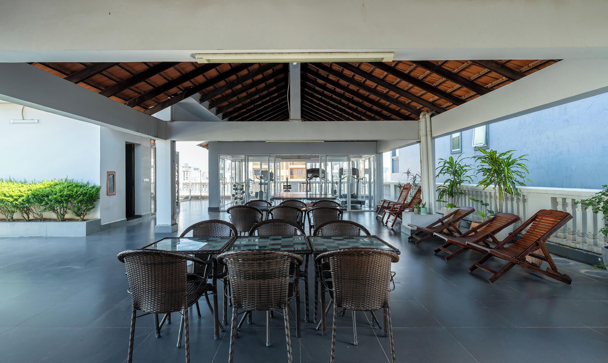 Un área de comedor al aire libre con una mesa de vidrio y sillas de mimbre, techo de madera y vista al mar.