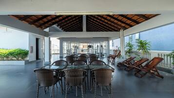 Un área de comedor al aire libre con una mesa de vidrio y sillas de mimbre, techo de madera y vista al mar.