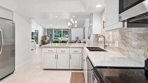A modern kitchen with a large island, stainless steel appliances, and a view to the outdoors. - NEW! Mariposa Hideaway by GPM -Chic Ironwood CC Condo (Palm Desert)