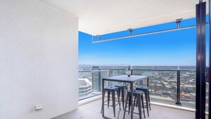 A balcony with a table and stools, a clear view of the cityscape, and a blue sky. - Circle on Cavill River View (Surfers Paradise)