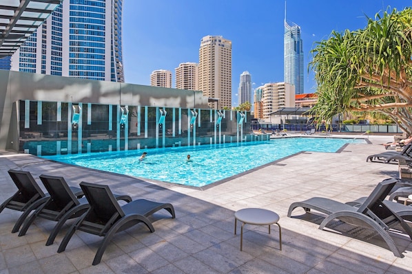 A swimming pool with lounge chairs, a small table, and a city skyline in the background.