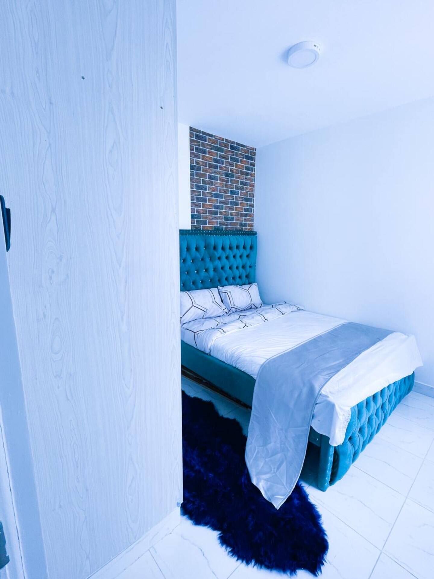 Een slaapkamer met een gestuukt hoofdeinde, een muur met baksteenmotief en een witte dekbedovertrek.