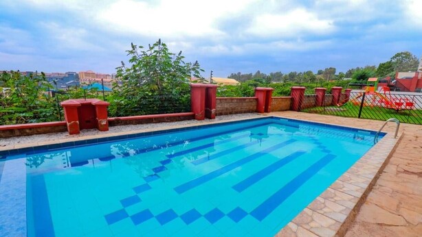 Una piscina rectangular con baldosas azules, rodeada por un borde de piedra y una valla roja.