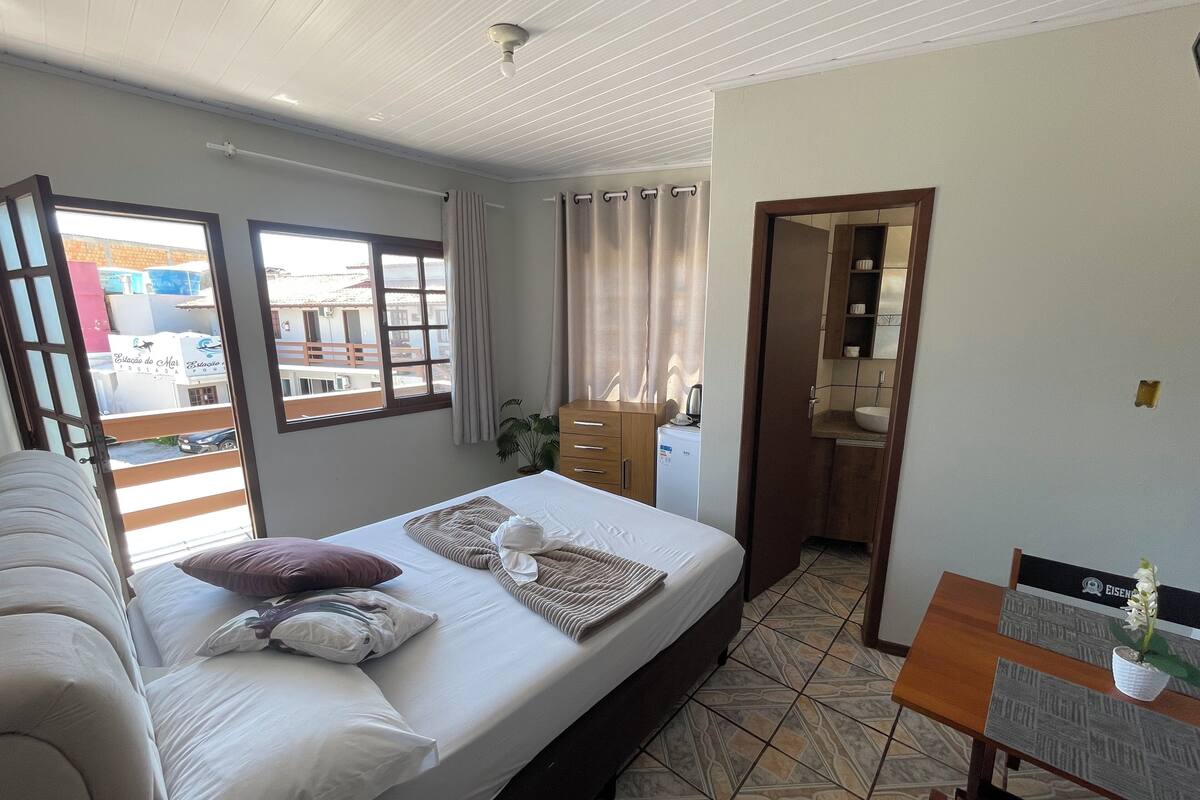 Ett hotellrum med en säng, ett skrivbord, en stol, ett litet bord, en krukväxt och ett badrum som syns genom en öppen dörr.