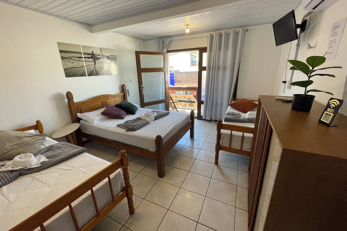 Ett hotellrum med två sängar i trä, ett litet bord, en tv, en växt och en balkong med gardiner.
