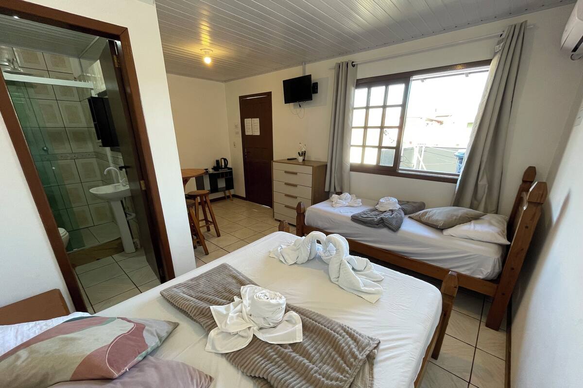 Ett hotellrum med en säng, ett skrivbord, en stol, en byrå, en tv och ett fönster med gardiner.