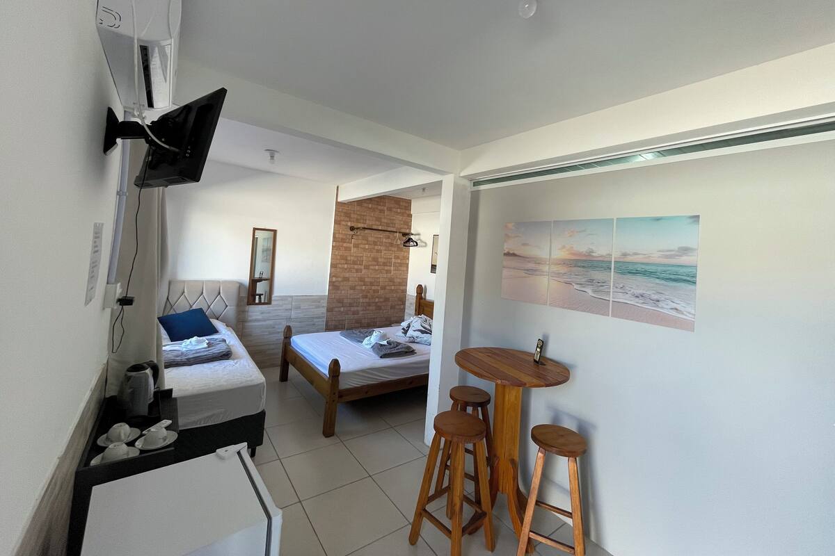 Ett kompakt hotellrum med en säng, ett litet bord med stolar, en spegel och en TV som är monterad på väggen.