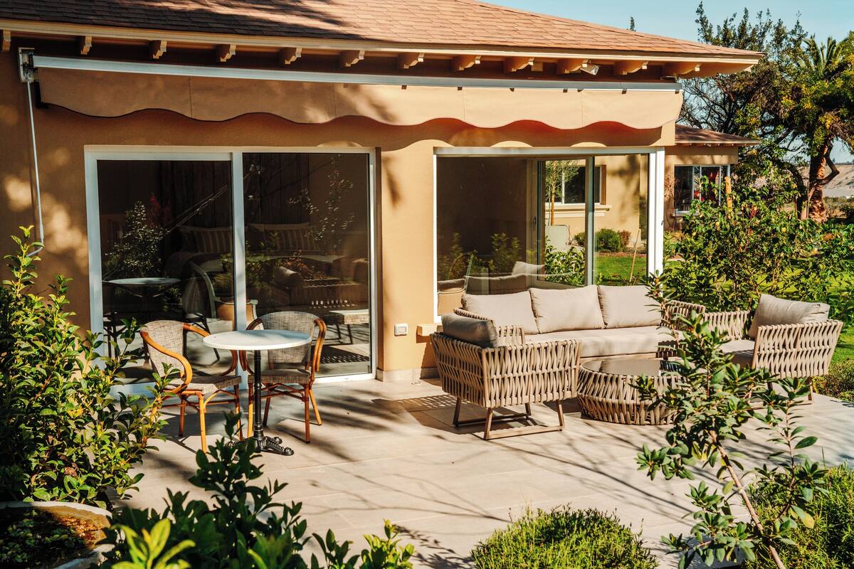 Eine überdachte Terrasse mit Gartenmöbeln, darunter eine Couch und Stühle sowie ein Tisch.
