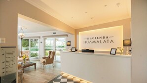 A reception area with a check-in counter, a seating area with chairs, and a floor plan sign. - Hacienda Huamalata (Ovalle)