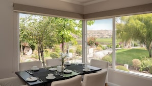 A dining area with a table set for four, large windows offering a view of a landscaped garden and distant hills. - Hacienda Huamalata (Ovalle)