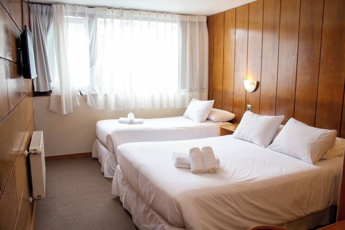 A hotel room with two beds, a TV, a window with curtains, and a wooden wall.