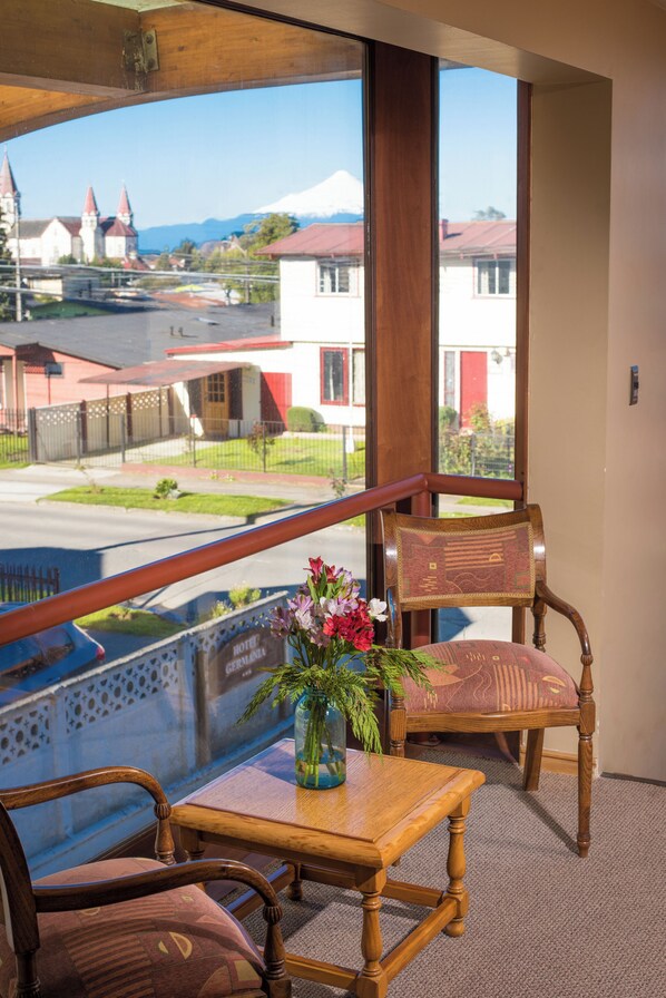 Ein Balkon mit Holztisch und Stühlen, einer Blumenvase und Blick auf Gebäude sowie einen Berg.