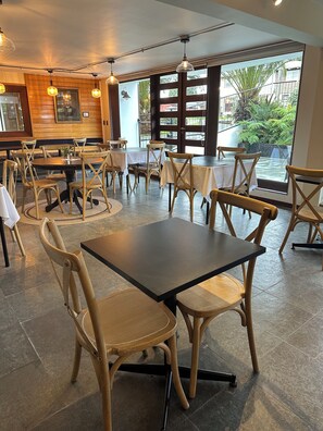 A restaurant interior with round tables, wooden chairs, and pendant lighting. - Hotel Germania (Puerto Varas)
