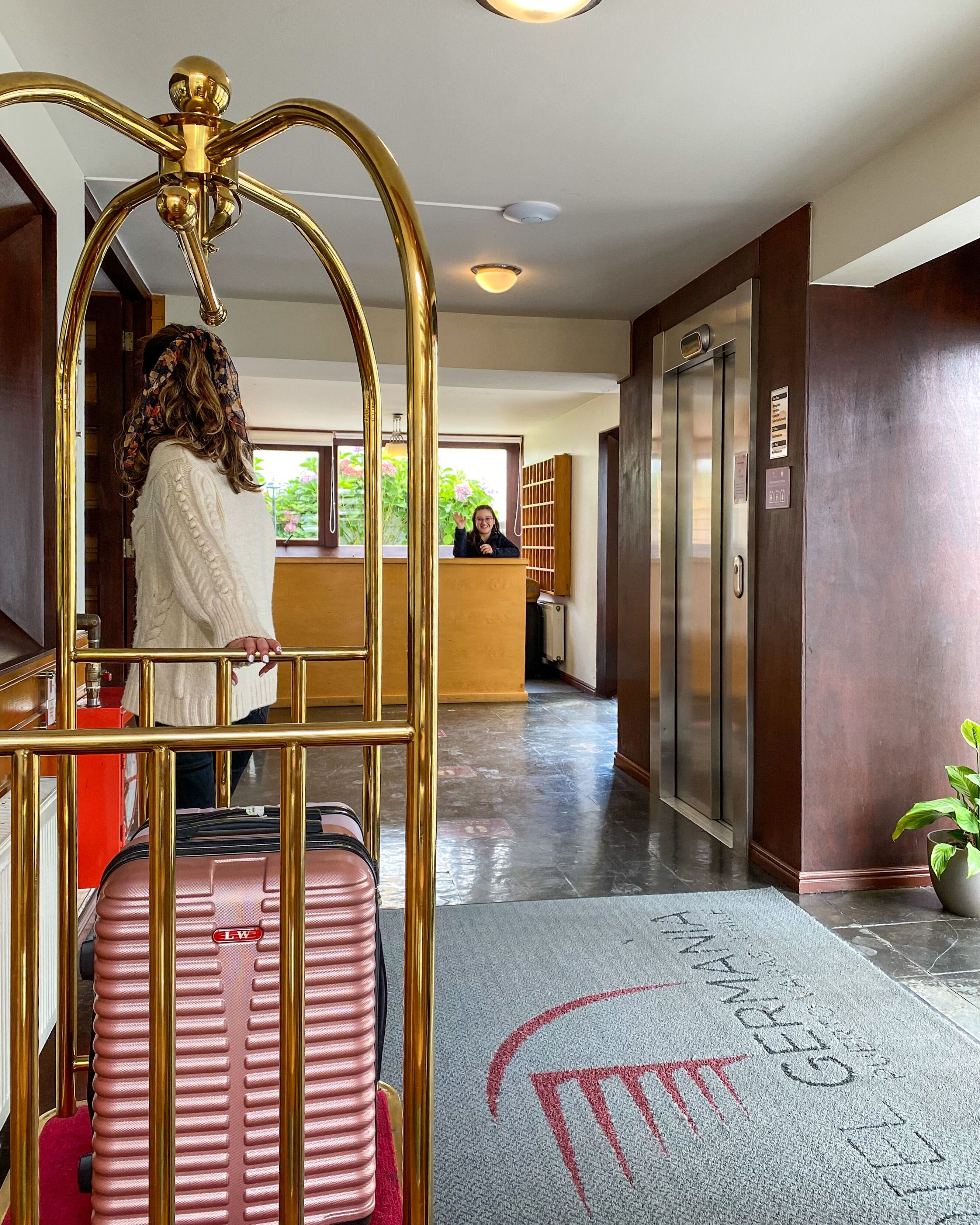 Un hall de hotel con mostrador de recepción, un ascensor y un atril para equipaje.