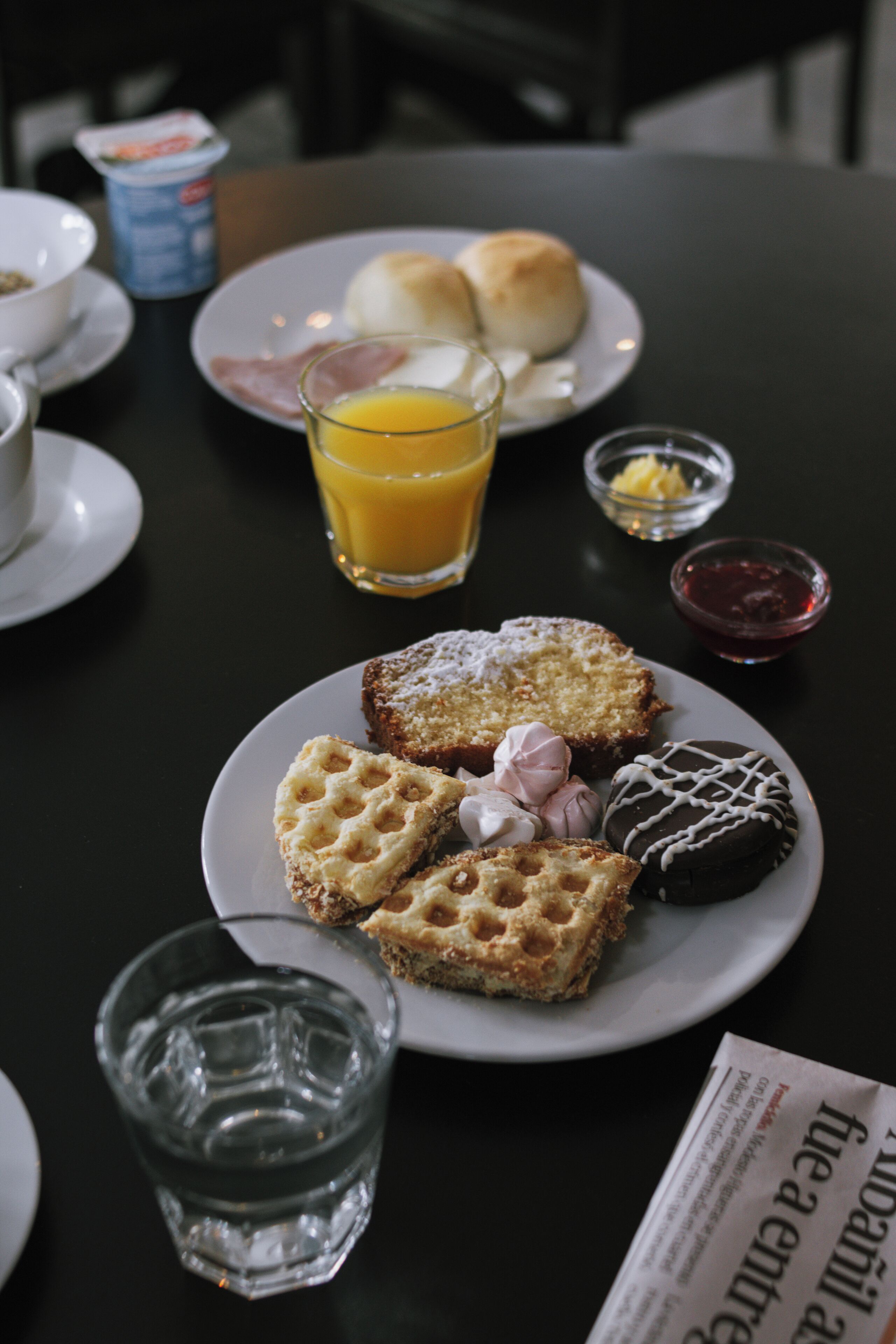 A breakfast setting with waffles, pastries, and a glass of orange juice on a table.