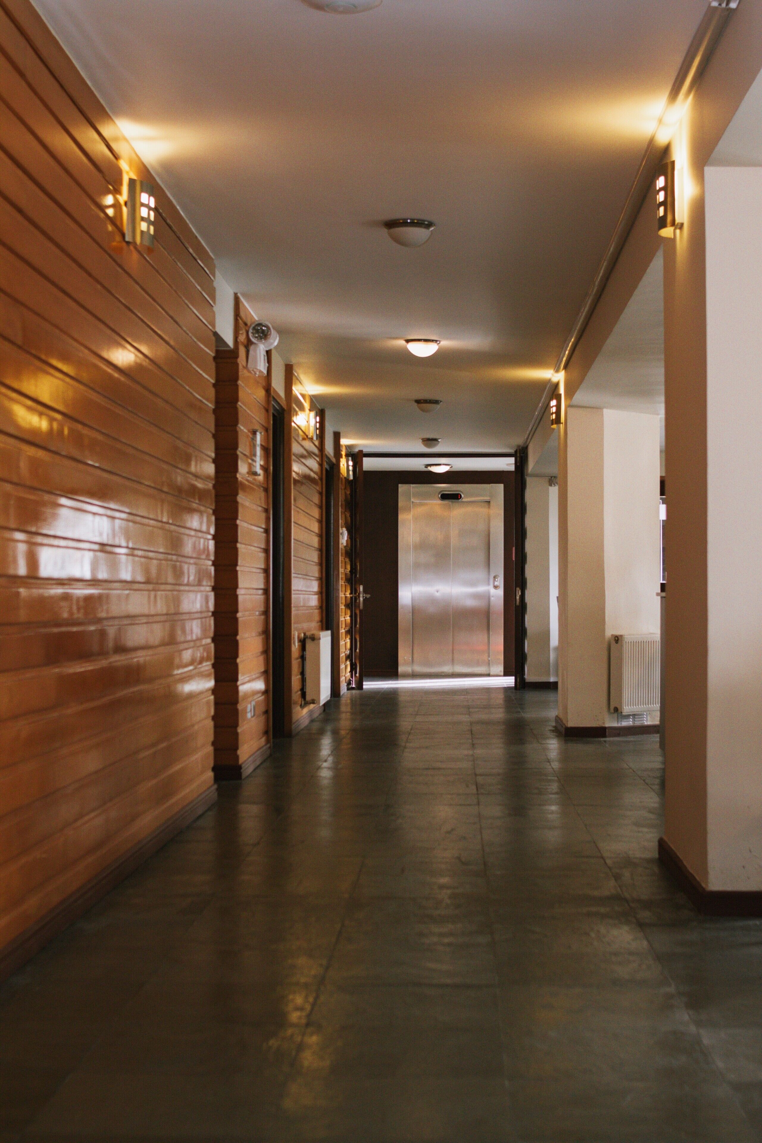 A hallway with wooden paneling, a ceiling light, and an elevator.