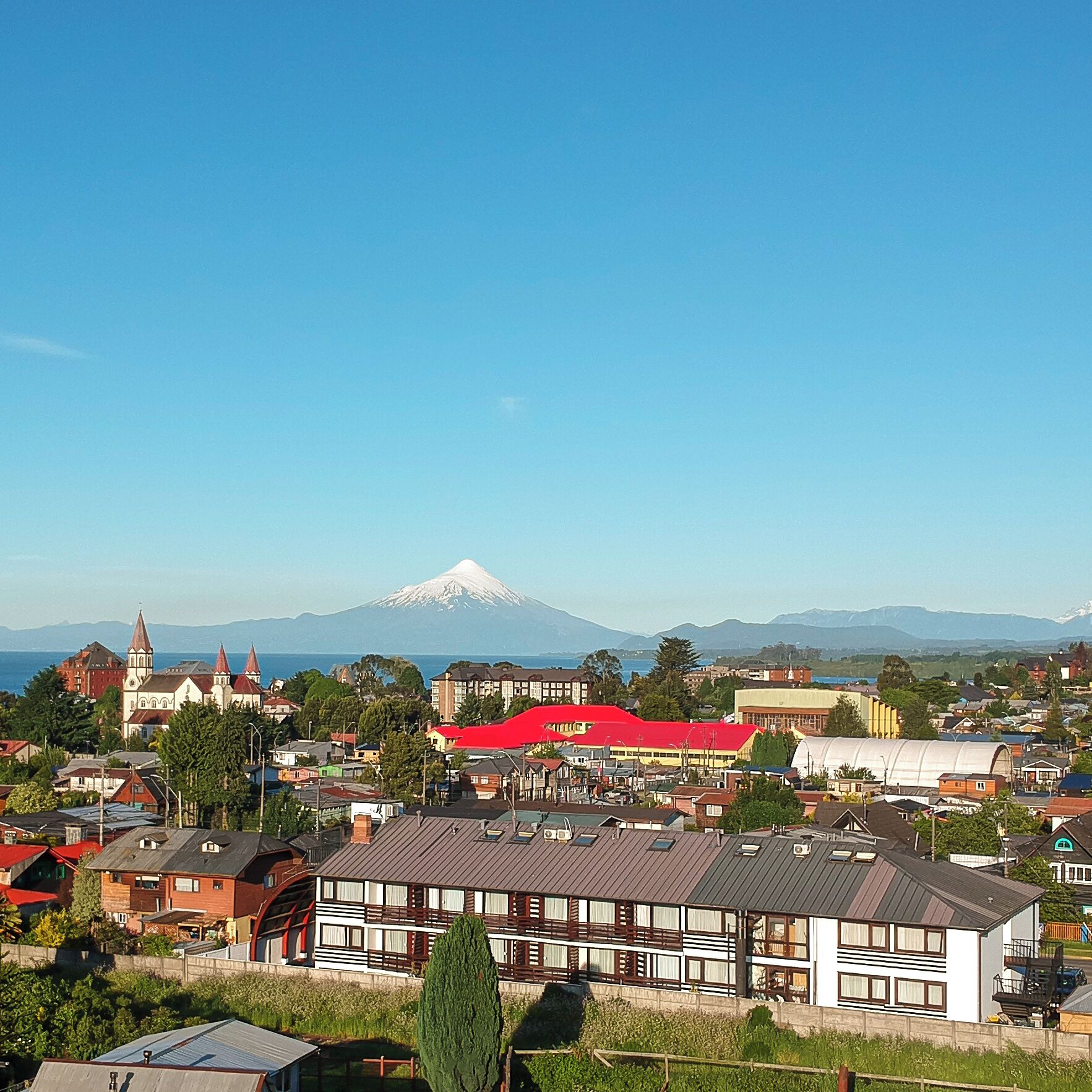 A town with a prominent church, a large red-roofed building, and a mountain in the background.