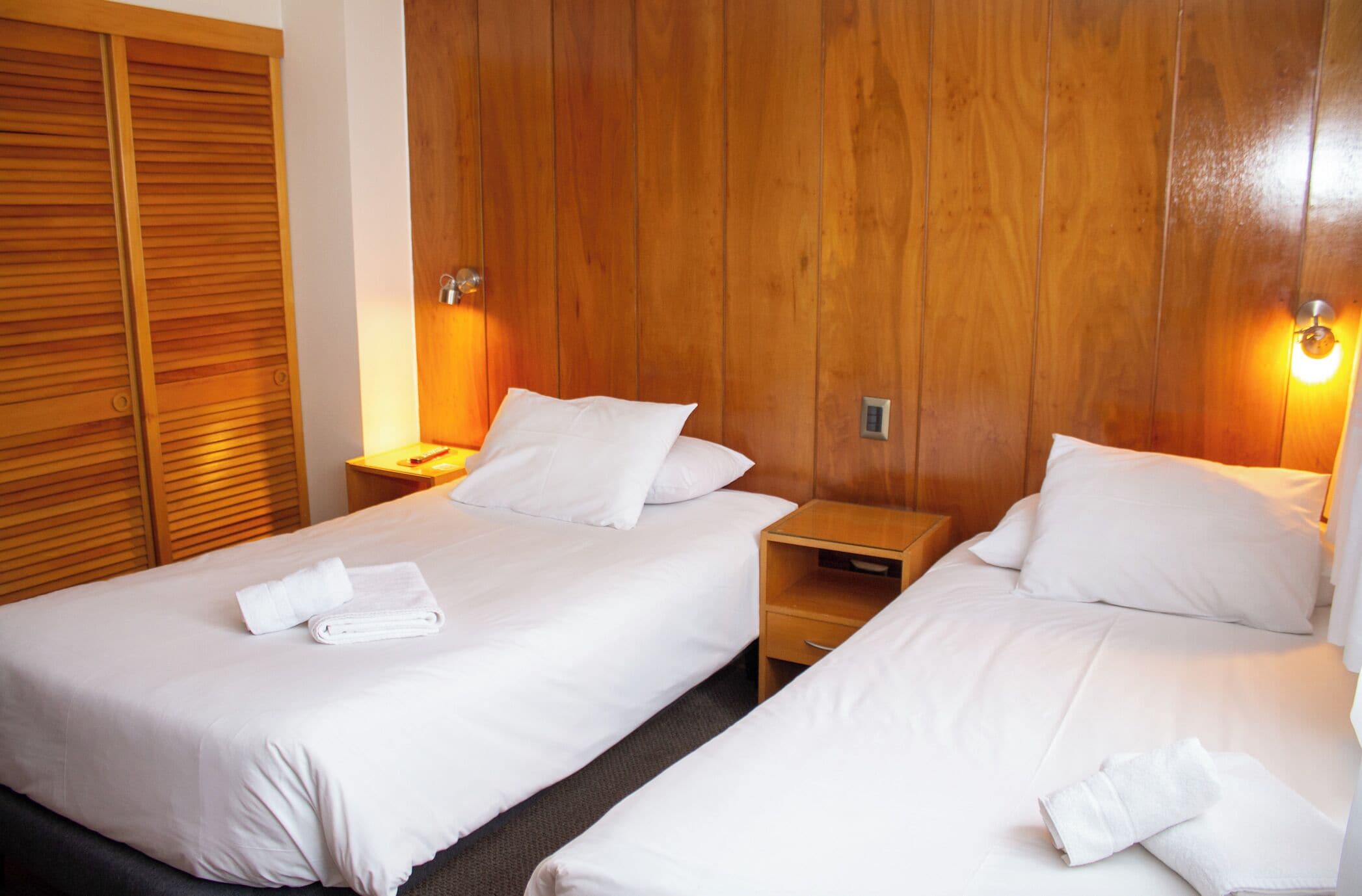Ein Hotelzimmer mit zwei Betten, einem Holzkopfstück, Nachttischlampen und einem Holzschrank.