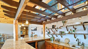 Une cuisine avec des poutres en bois, des plans de travail en granit et des luminaires suspendus.