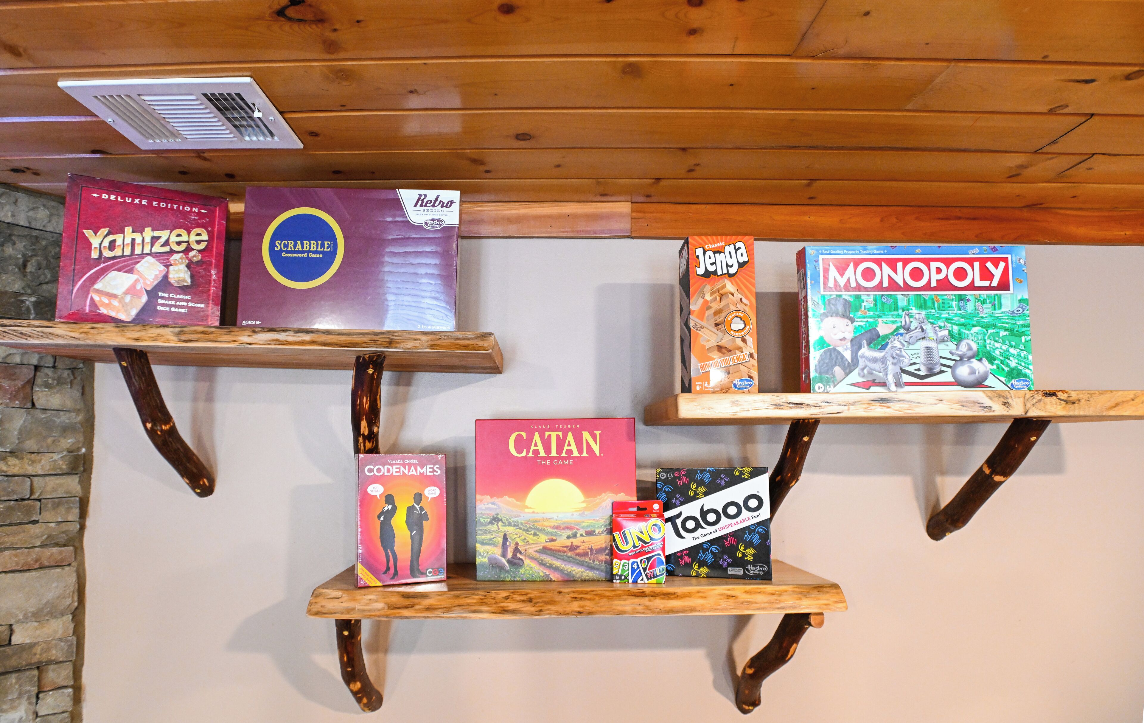 A wooden shelf with various board games including Catan, Monopoly, and Scrabble.