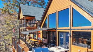 Une maison en bois à plusieurs niveaux, dotée d’une terrasse, d’un espace salon extérieur et d’un coin barbecue.