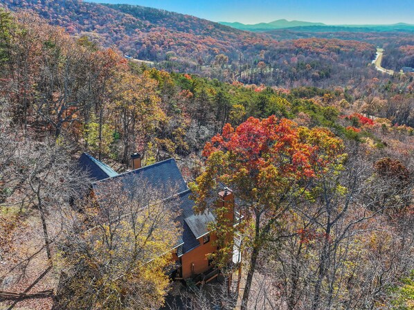 Une maison entourée d’un feuillage automnal, avec vue sur des montagnes lointaines.