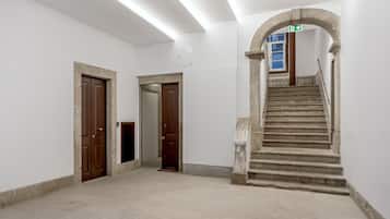 Um corredor com escadas, uma porta de madeira e uma parede branca.