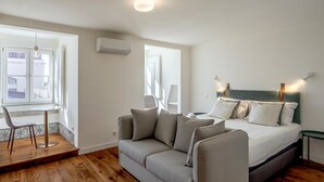A modern bedroom with a grey sofa, a bed with white bedding, and a small table with a chair. - Bairro Alto Garden With A View by Homing (Lisbon)