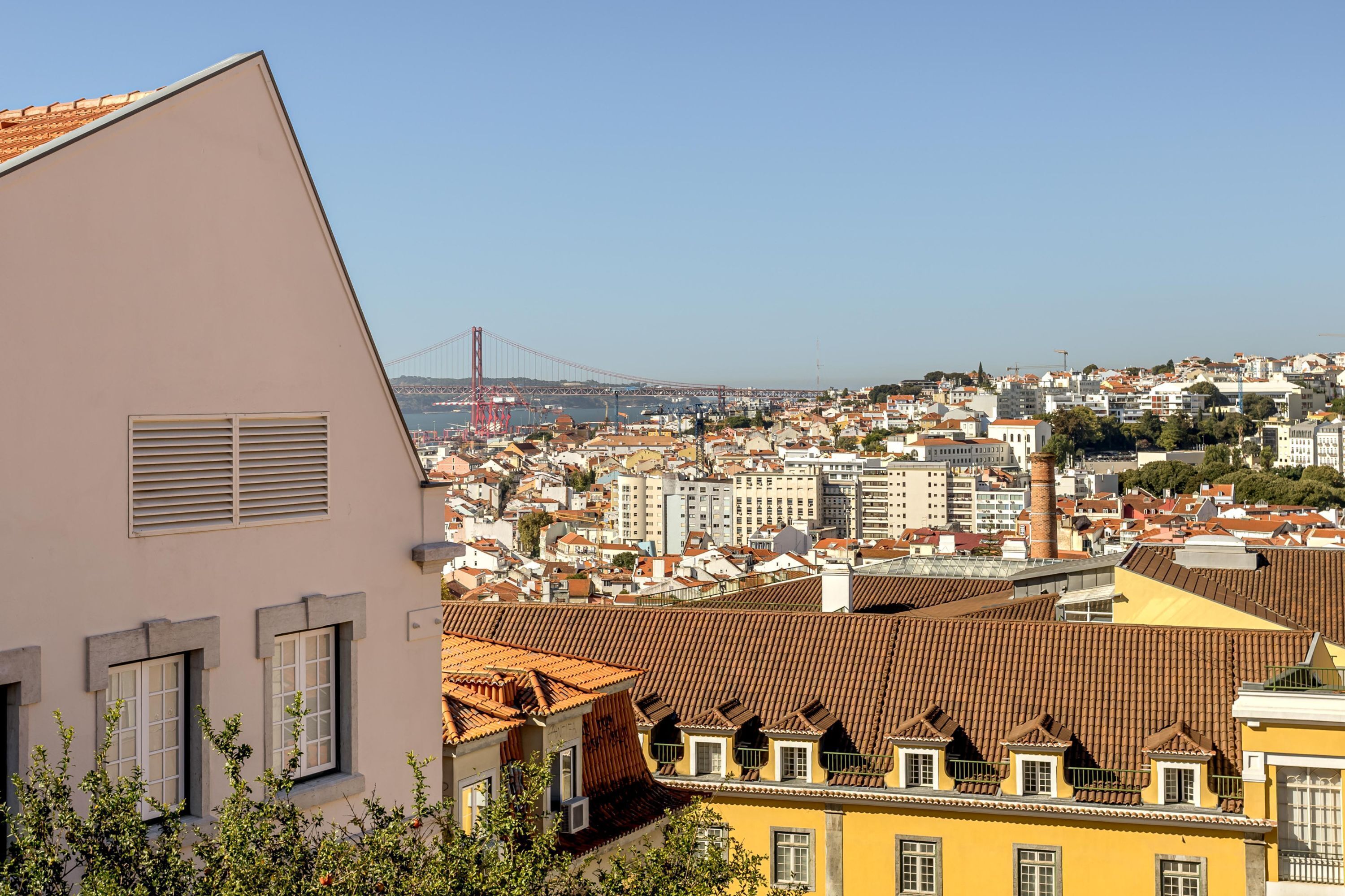 Un paisaje urbano con un puente rojo destacado al fondo, diversos edificios y un edificio amarillo en primer plano.