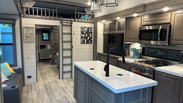 A modern kitchen with a central island, built-in appliances, and a loft bedroom with a bunk bed. - Visit Cumberland Falls, see the Moonbow and enjoy Corbin's luxury RV campground. (Corbin)