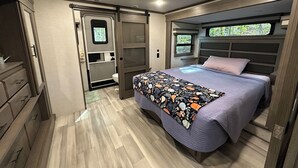 A compact RV bedroom with a bed, dresser, and a small bathroom. - Visit Cumberland Falls, see the Moonbow and enjoy Corbin's luxury RV campground. (Corbin)