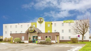 A B&B hotel with a distinct yellow and white facade, a green entrance, and a visible parking area. - B B Hotel Tours Centre Commercial La Petite Arche Hotel (Tours)