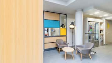 Een moderne lobby met een receptiebalie, twee fauteuils, een kleine tafel en een glazen scheidingswand.