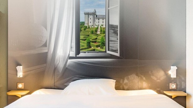 A bedroom with a large window, a bed, bedside lamps, and a view of a castle. - B B Hotel Tours Centre Commercial La Petite Arche Hotel (Tours)