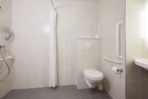 Een badkamer met een douche, toilet en handgrepen.